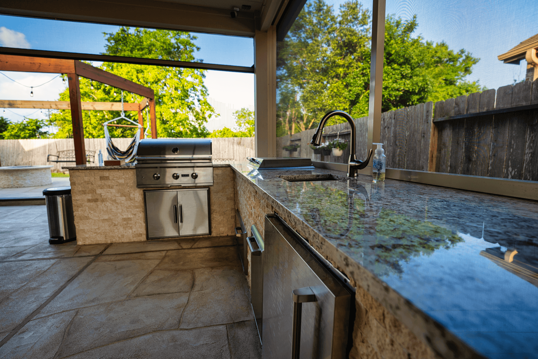 Outdoor kitchen grill and sink area underneath a covered patio