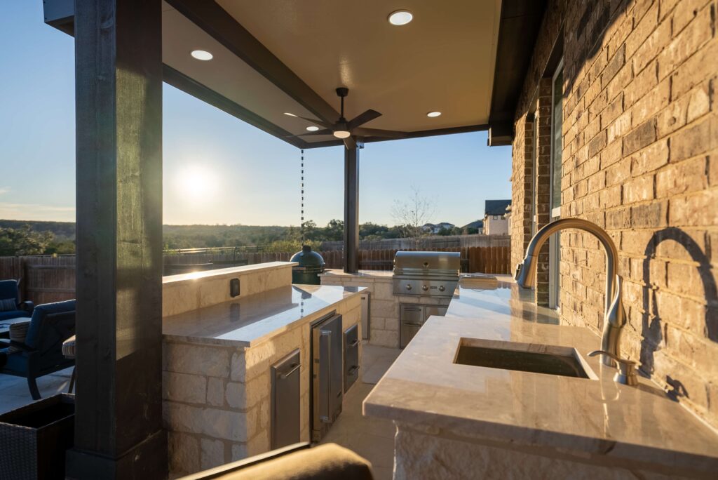 Outdoor kitchen with grill area and stone wall under patio