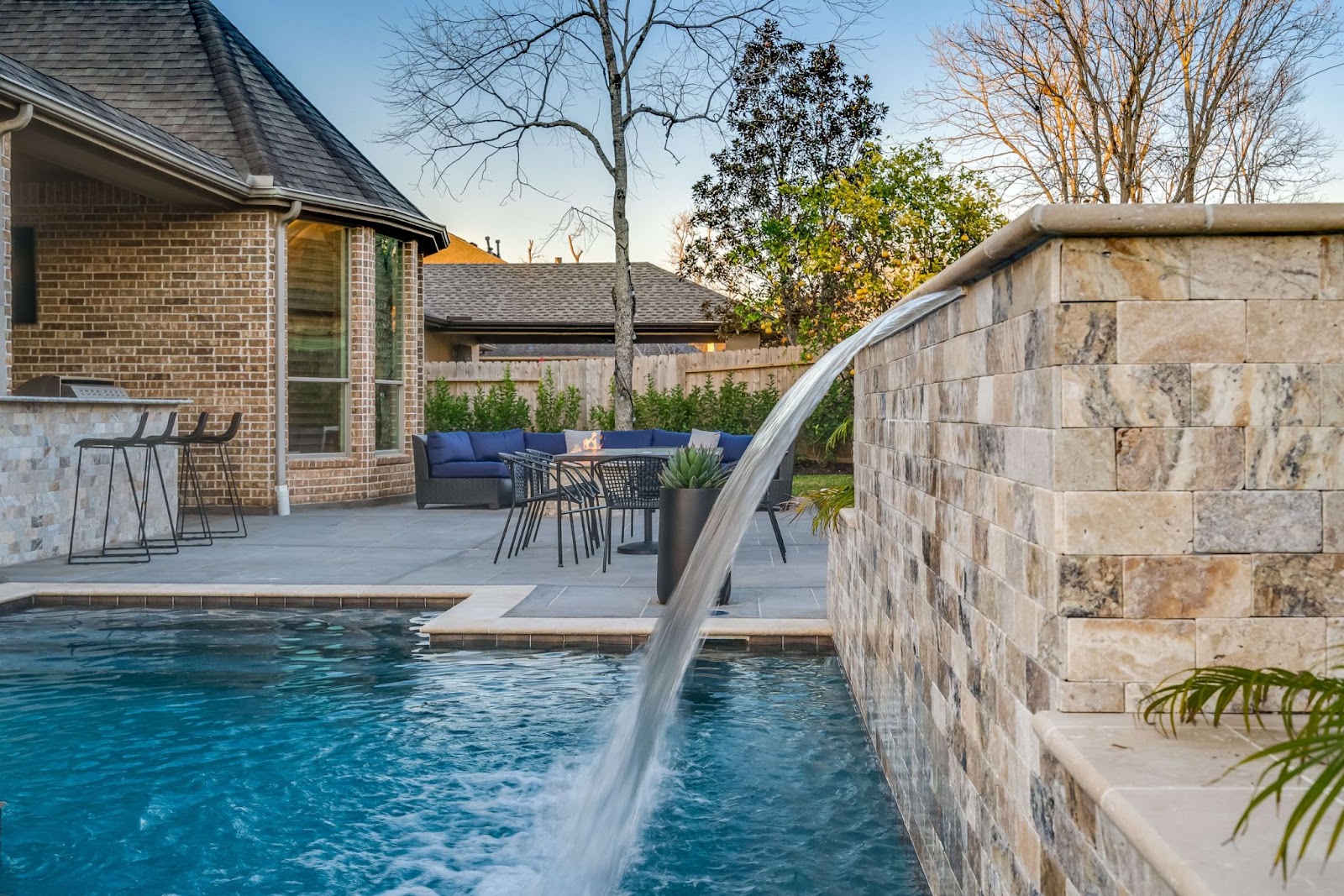 natural stone water feature cascades into texas backyard swimming pool