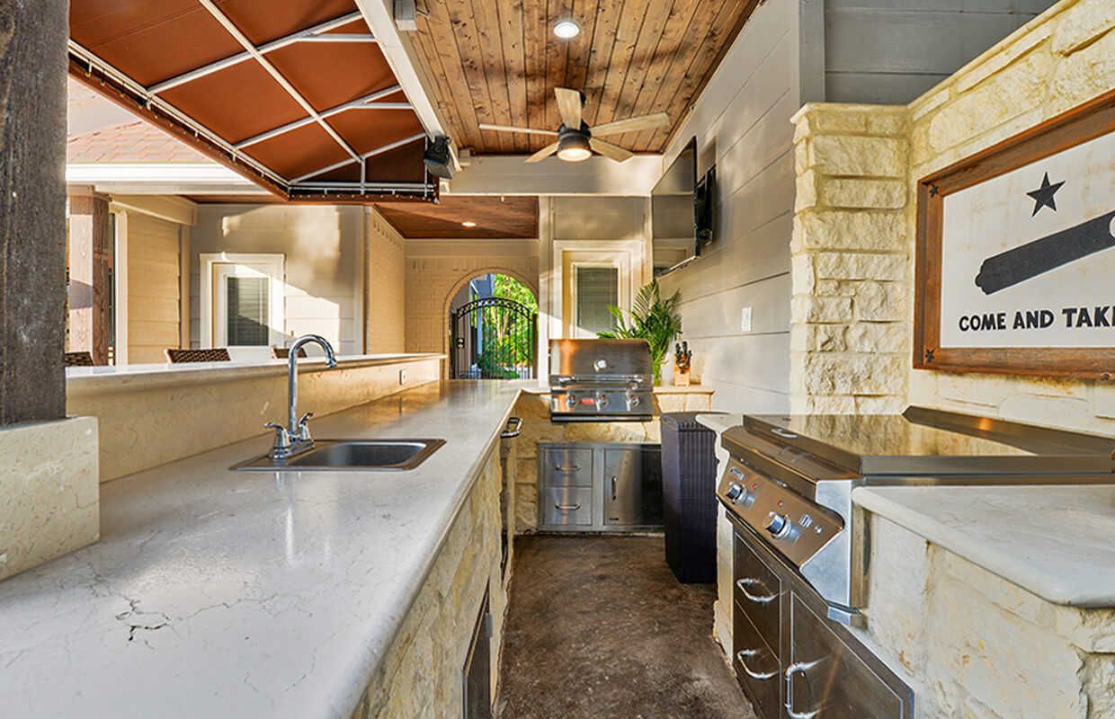 light colored outdoor kitchen on covered patio with white countertops and full stove