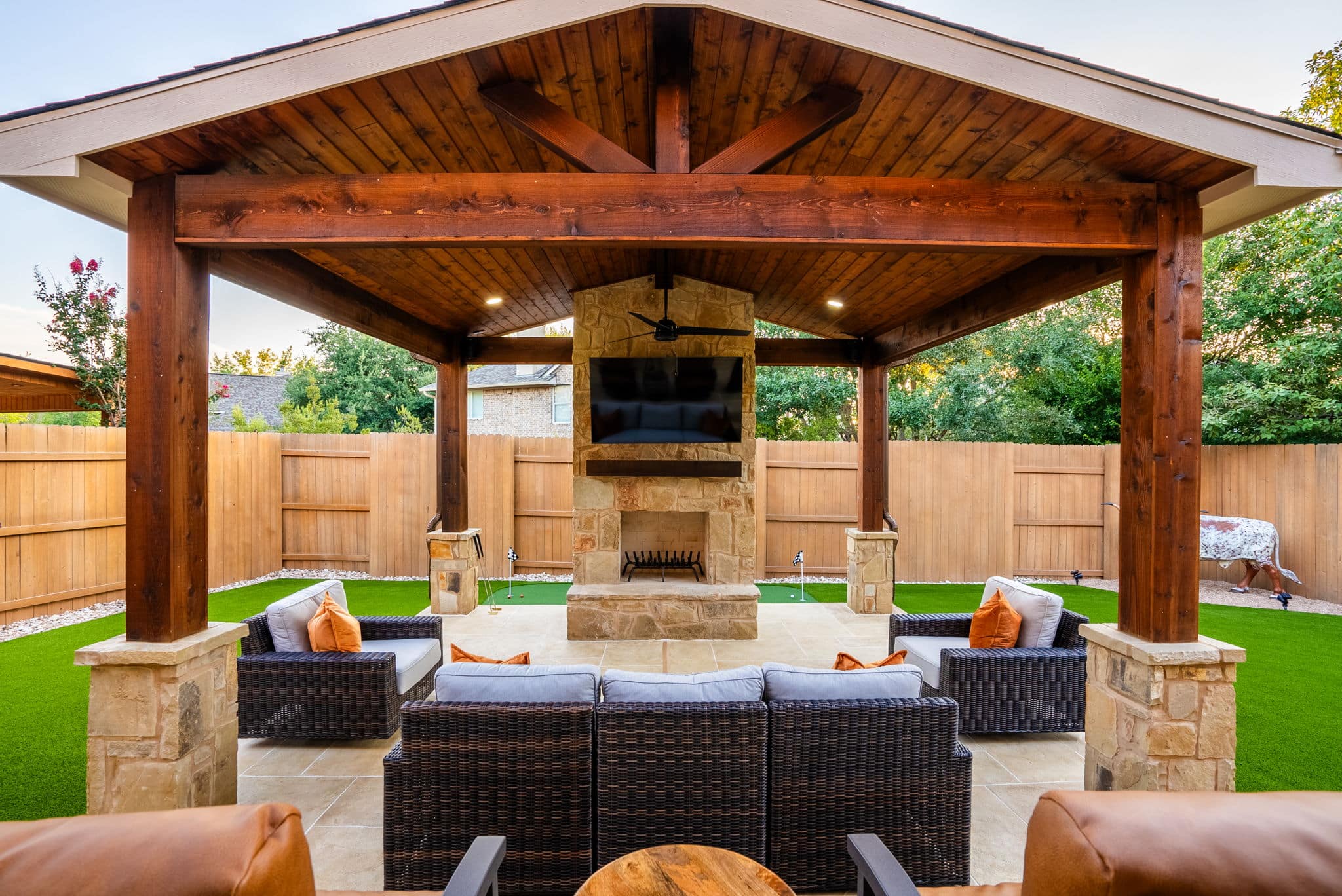 Artificial turf backyard with covered patio and stone fireplace